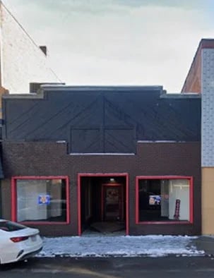 Modern storefront with red-framed windows and dark blue awning, brick and metal facade